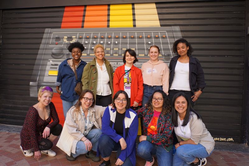 a diverse group of women and nonbinary people smiling in front of a mural of the Roland 808